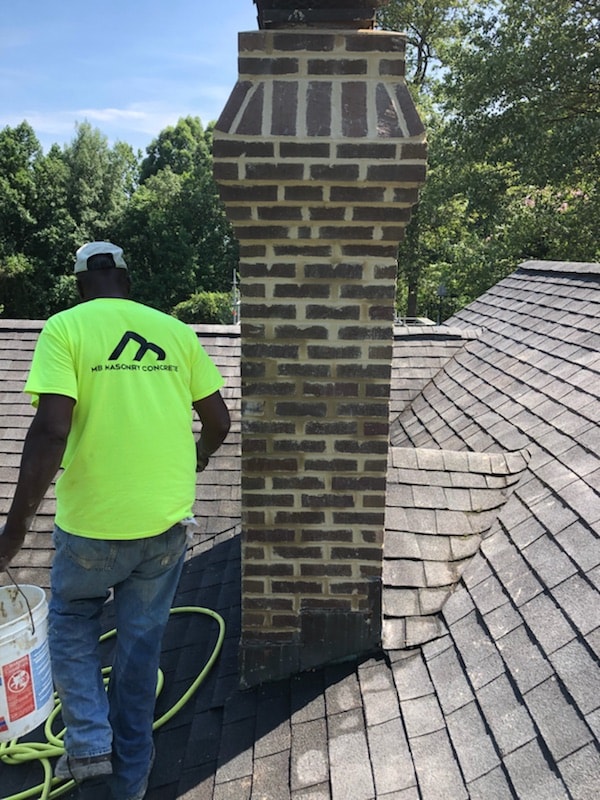 Masonry worker repairing a brick chimney on a roof