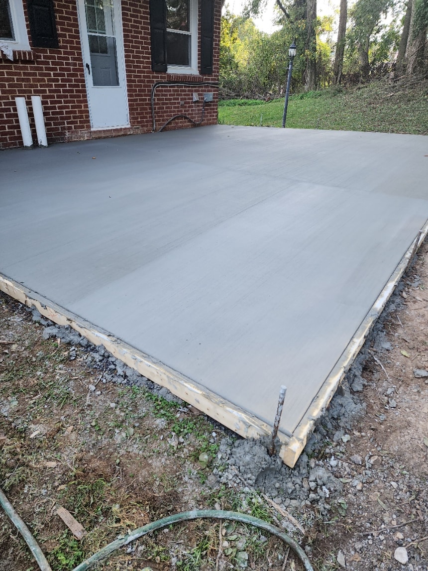 Freshly poured concrete patio beside a brick home