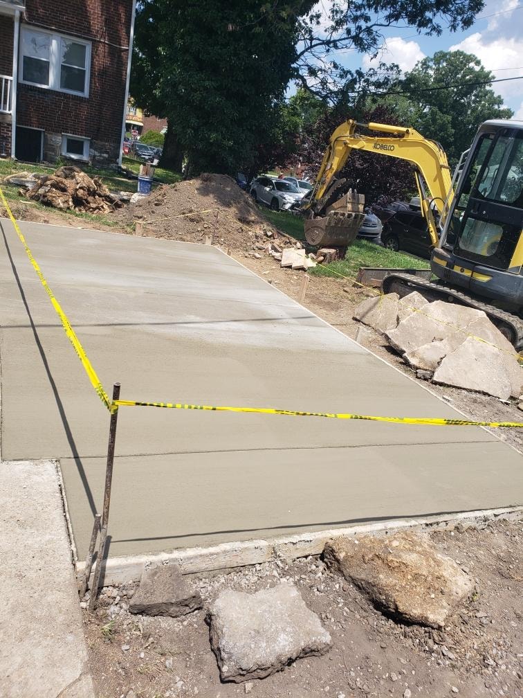 Fresh concrete pavement beside an excavator at a residential project