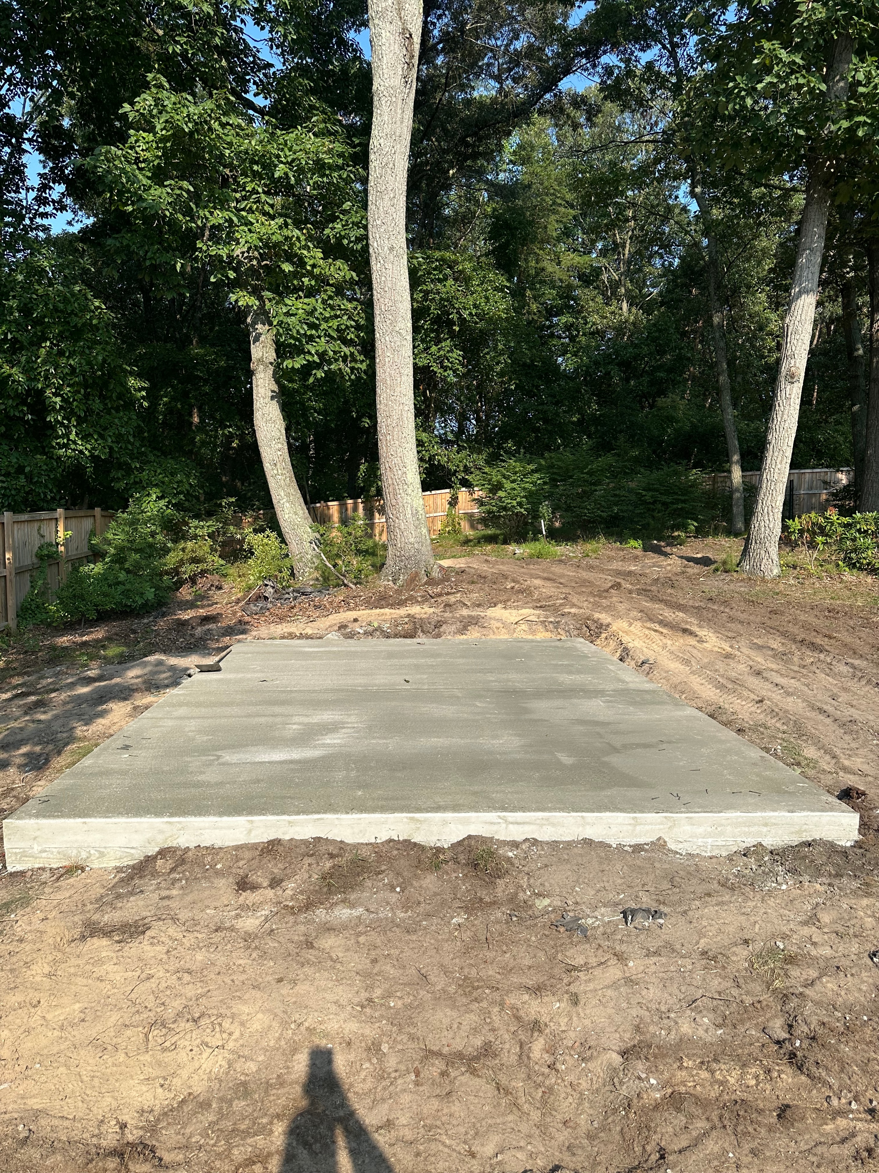 Freshly poured concrete slab in a wooded backyard